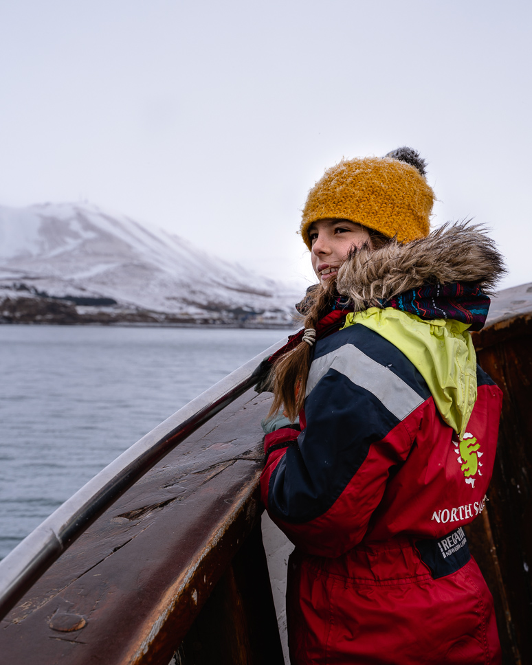 Meisje kijkt vanop een boot in winterkledij over de zee op zoek naar walvissen in IJsland