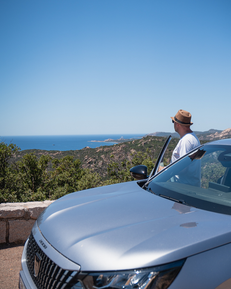 Man looks out at the sea from a car during a road trip in Corsica.